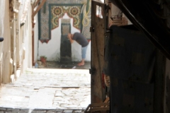 A man in front of the door to a Mosque entrance in the Casbah beginning the rite of washing his hands, feet and other areas of the body before entering the Mosque to pray.