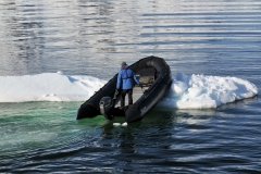 A zodiac and driver forcefully pushing an iceberg away from the aft part of the ship.