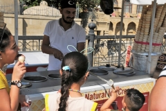 Selling ice cream is an art and a game. Here a young boy tries to take the ice cream cone from the vendor.  The vendor twirls and pulls the ice cream cone back and forth. It is a fun time to watch the children laugh and try to catch the ice cream cone.
