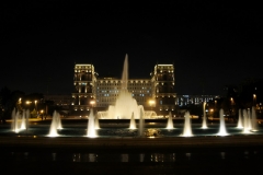 Old Soviet Block Building lighted up with the fountains across the street from the building.
