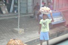 Young boy working and carrying food  balanced on his head.