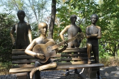 Iconic bench statue of the Beatles at a park at the top of a hill overlooking the city of Almaty.  The composition of the monument represents a bronze bench on which sits John Lennon playing the guitar, surrounded by the other members of the band standing: Paul McCartney, Ringo Starr and George Harrison. Songs by The Beatles are constantly played from speakers.