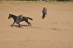Here we see a rider attempting to pick up a bag left on the ground while riding his horse.