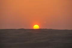 The sun setting into the desert dunes