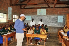 In this photo you can see the two teachers in the white smocks at the rear of the room .  Look at the black board packed with work for the students.  Sam is translating the questions from the students to us.