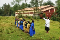 This class is  outdoors learning about the plants that are grown in the area. The teacher would hold up a plant and the kids would yell the name of the plant.
