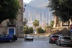 Peep a boo view of the harbor in Palermo through two buildings.  Sailboats  docked in the harbor.