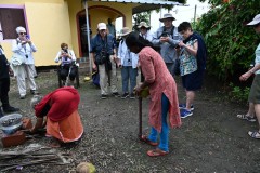 The mother of the family shows how they start a fire and boil mussels from the mud of the canal. The wife is beginning to cut up a coconut. 