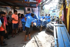 A group of men struggle to move these laundry bags through the tight areas on a dolly.  
