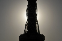 The sun setting behind the tower. The sun is showing off the sensational architectural, with its massive base and swirling lines and crown at the top.