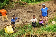 A young boy on a bicycle carrying water home for his family walking alongside.